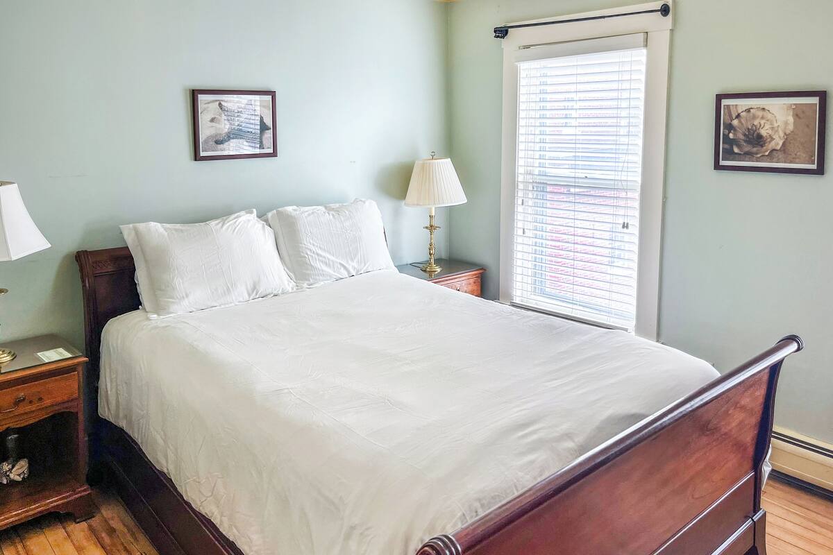 A bedroom with a wooden bed, a nightstand, a lamp, and two framed pictures on the wall.