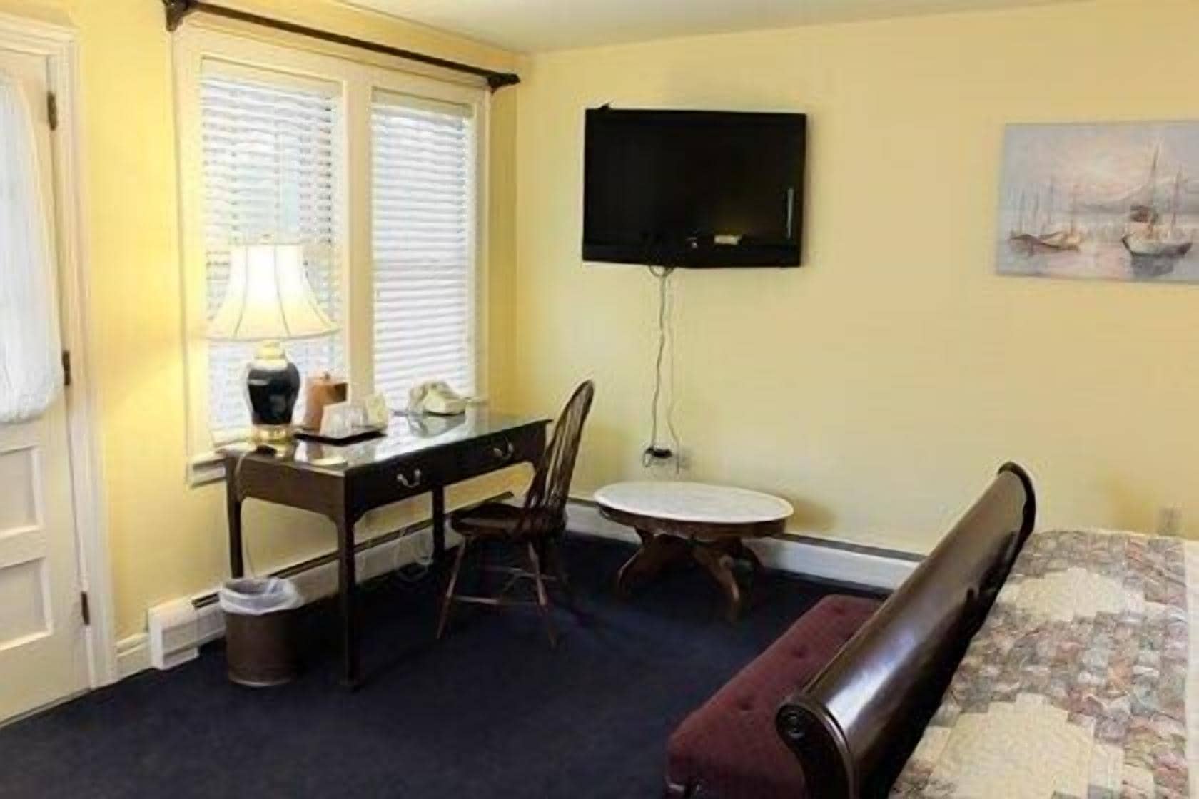 A hotel room with a desk, chair, round table, and a bed.