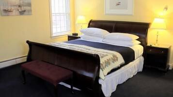 A neatly made bed with a headboard, a bedside table with a lamp, a bench, and a window with blinds.