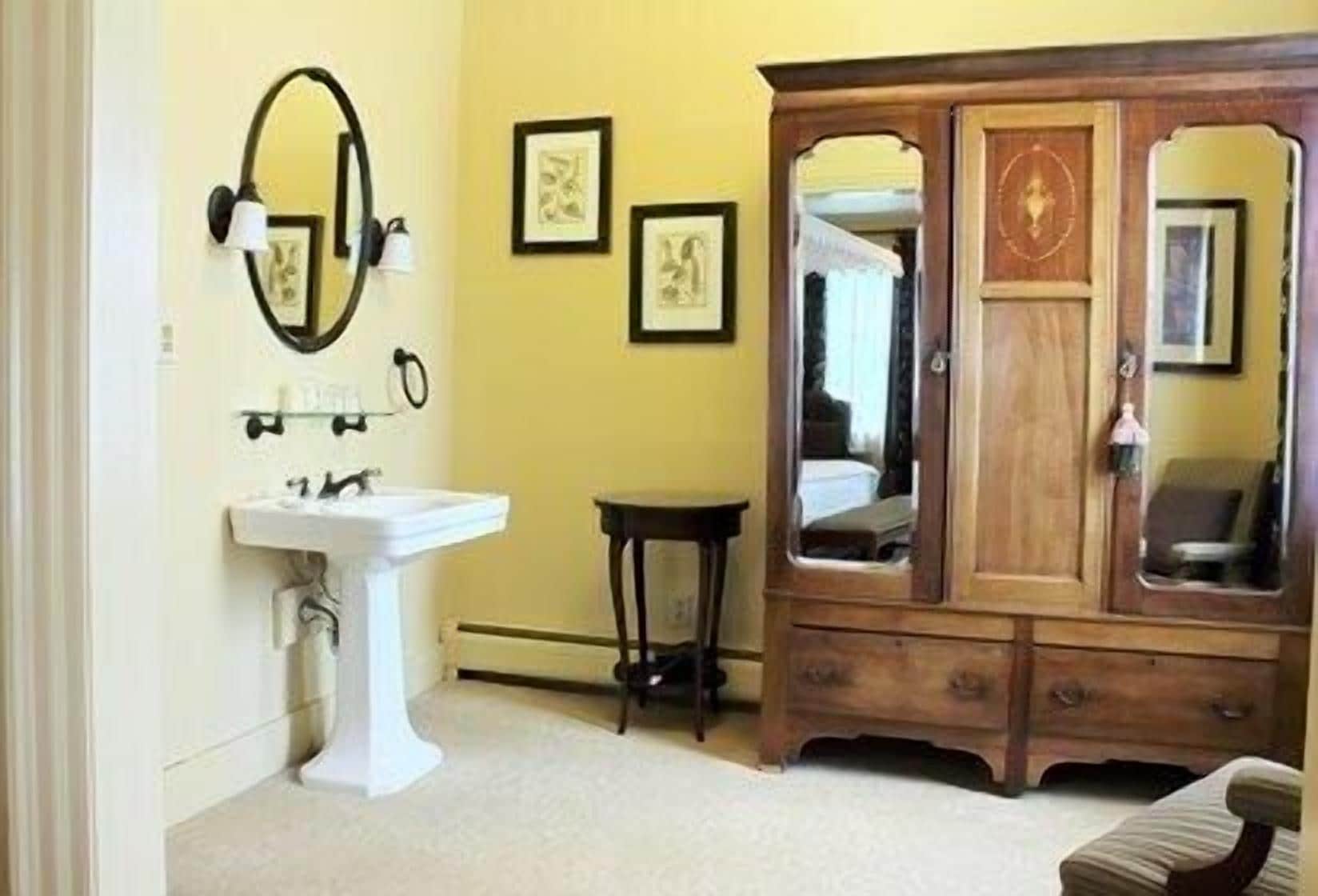 Une salle de bain avec un lavabo sur colonne blanc, un meuble en bois doté de miroirs et des œuvres d’art encadrées accrochées au mur.