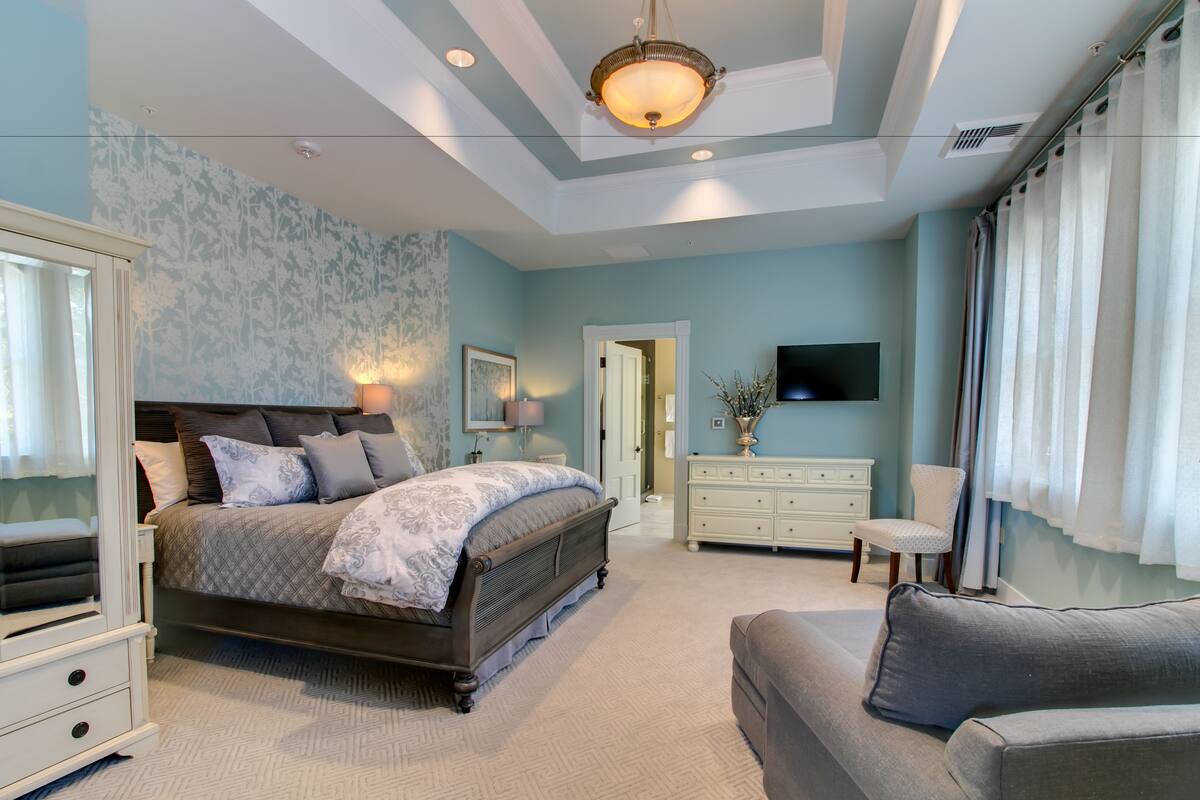 Un dormitorio con cama, cómoda, silla y televisor en la pared.