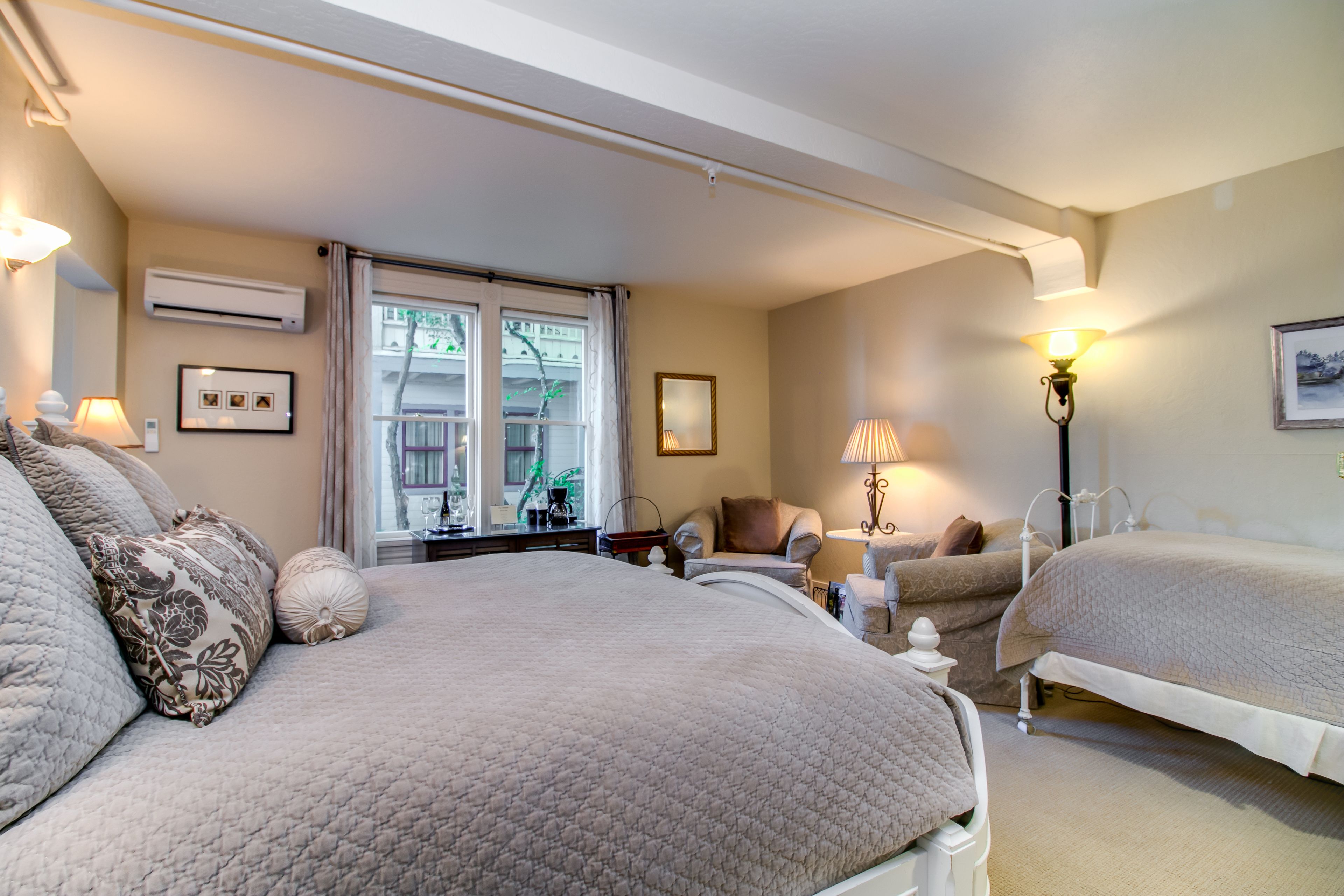 Une chambre d’hôtel avec deux lits, une fenêtre donnant sur un paysage agréable, une chaise, une lampe et un tableau au mur.
