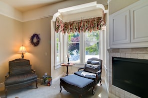 A cozy living room with a fireplace, a window with curtains, a lamp, and a chair.