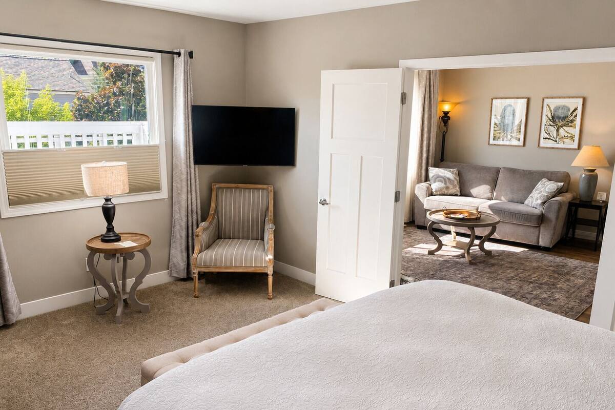 Una habitación de hotel con cama, sillón, sofá, televisor y lámpara.