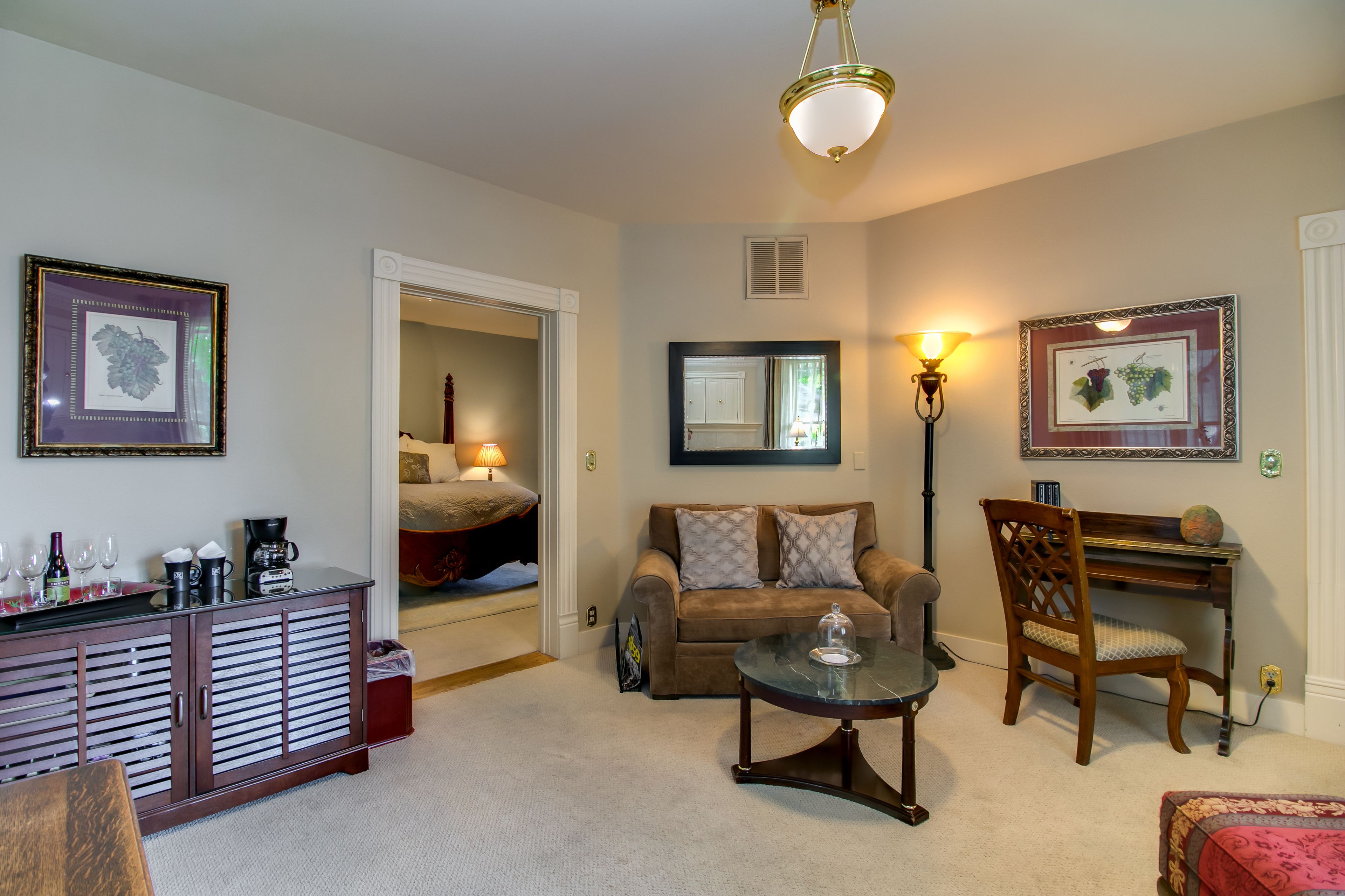 A cozy living room with a sofa, coffee table, and a piano. There are framed pictures on the walls and a cabinet with various items on top.