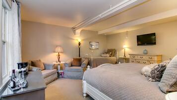 A hotel room with a bed, a sofa, a desk with a coffee maker, and a TV on the wall.