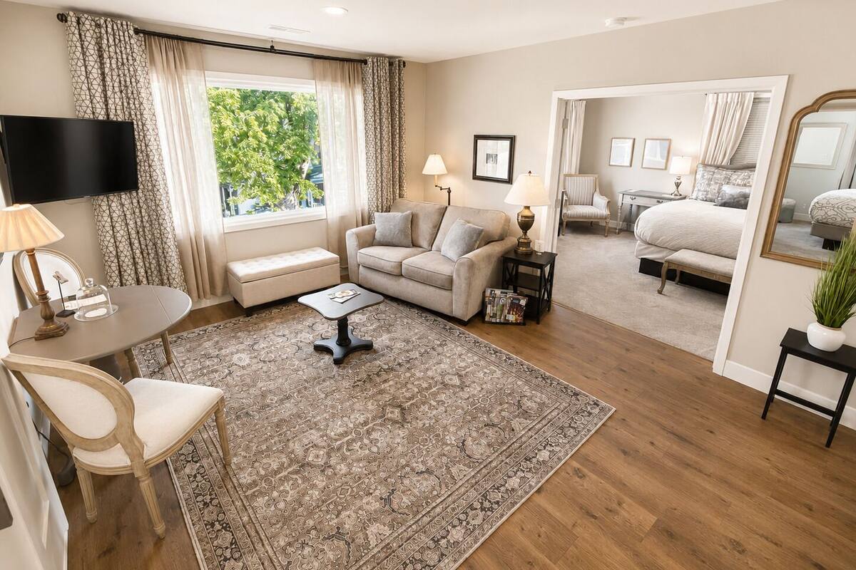 Una sala moderna con sofá, mesa de centro y televisor. Hay un ventanal con cortinas, un espejo y vista a un dormitorio.