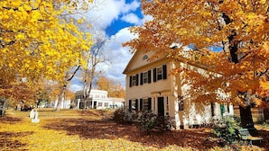 A two-story house with a porch and a garden area covered in yellow leaves. - Arlington Inn (Arlington)