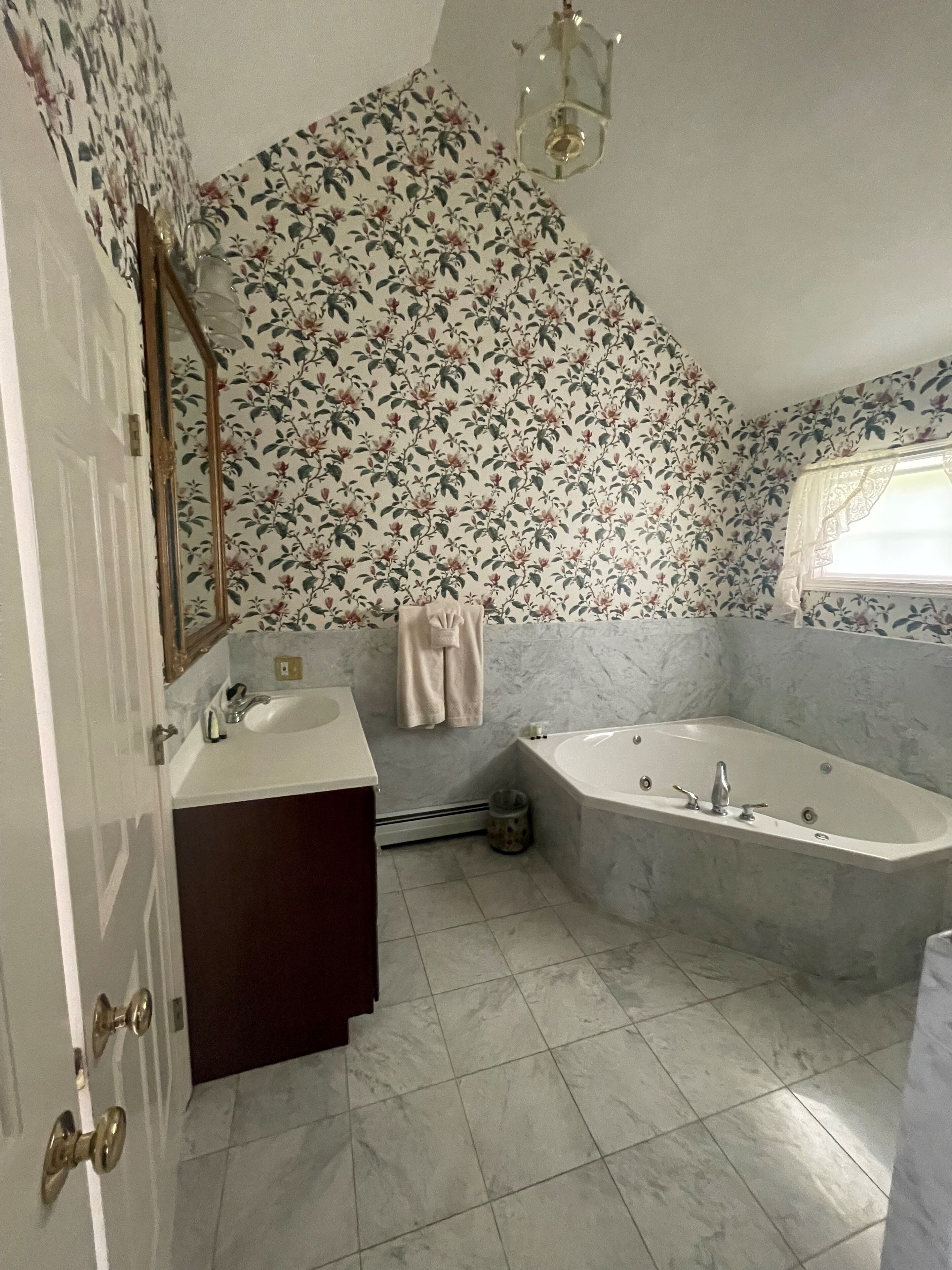 A bathroom with a large bathtub, a sink, a mirror, and a window.