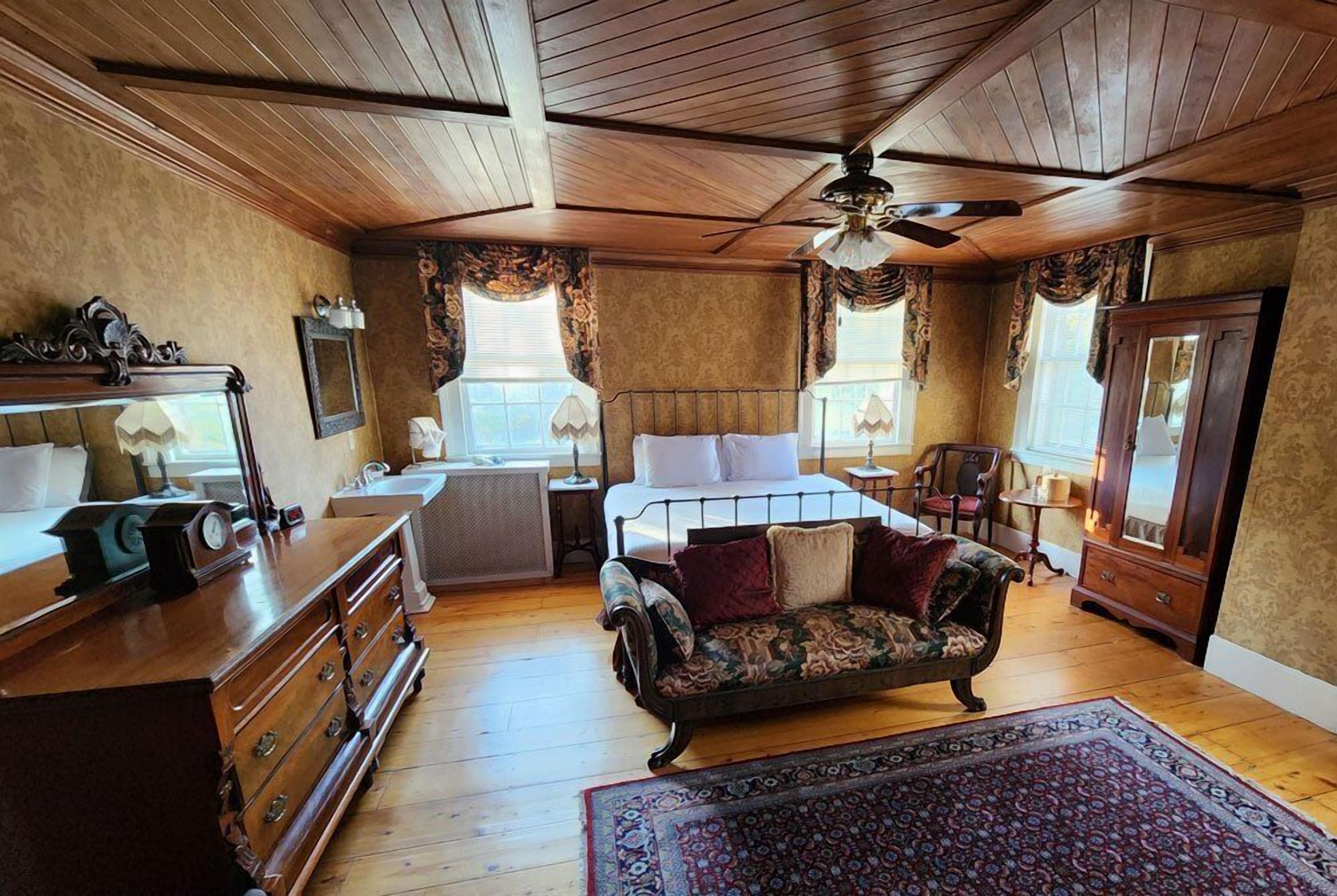 A traditional room with a bed, dresser, vanity, and a ceiling fan.