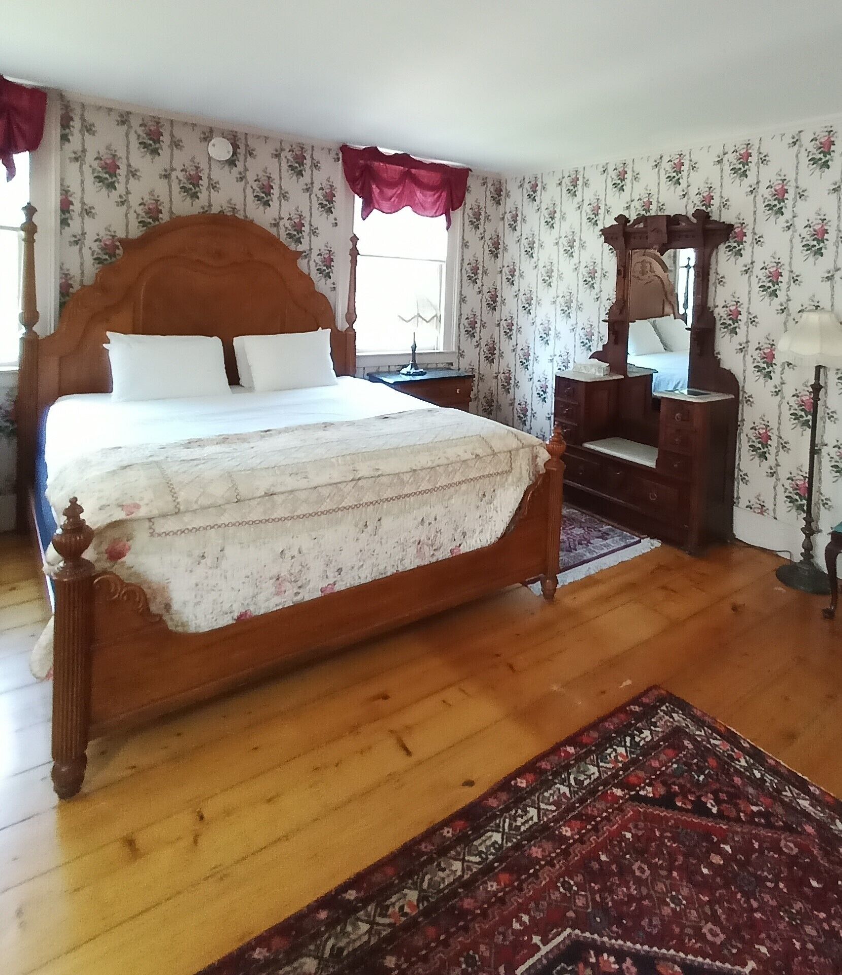 A bedroom with a wooden bed, a dresser, a mirror, and a patterned rug.