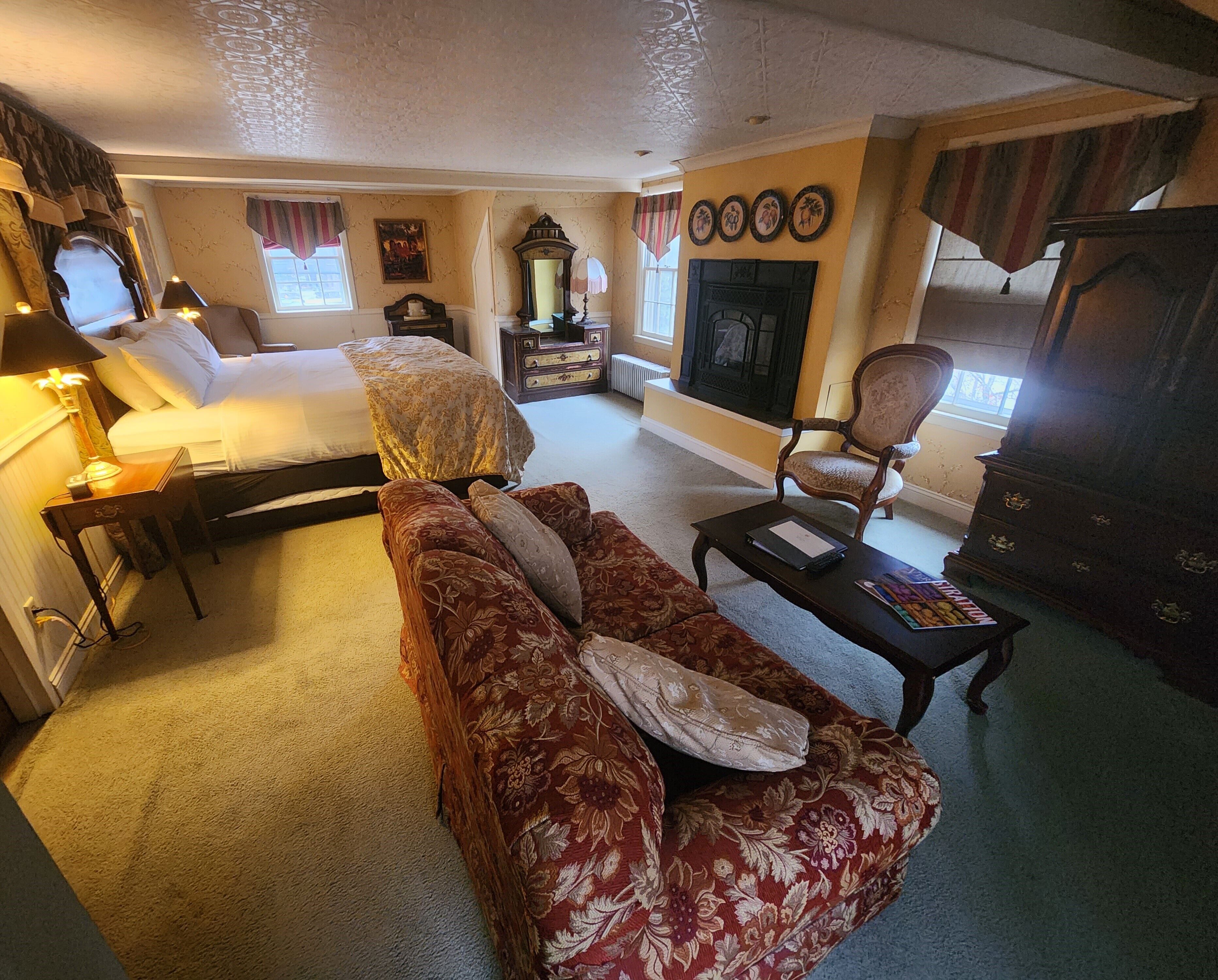 A well-appointed hotel room with a large bed, a sofa, a fireplace, and a television.