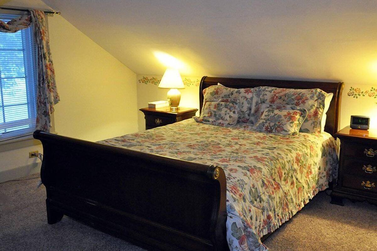 Une chambre à coucher avec un lit, une table de chevet, une lampe et une fenêtre avec des rideaux.