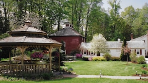 A gazebo, a red barn, and a white house in a garden with trees and flowers. - Arlington Inn (Arlington)