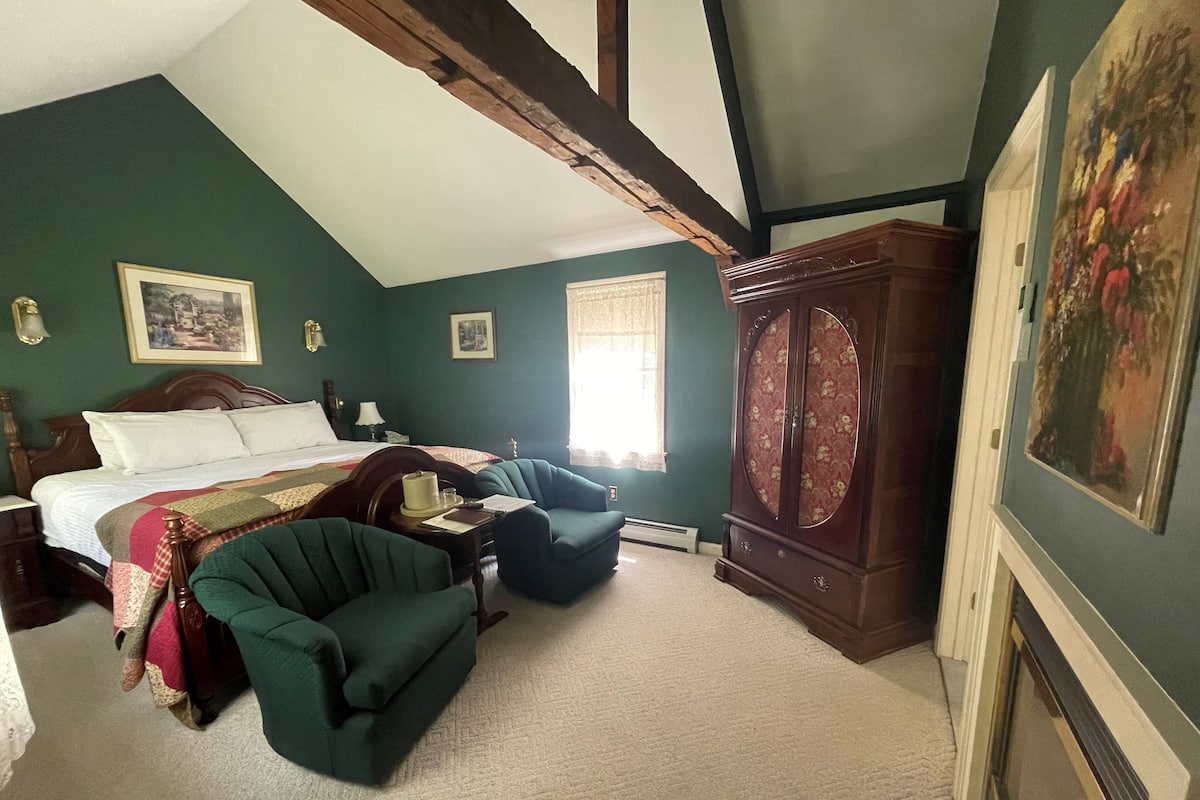 Une chambre à coucher avec un lit, deux fauteuils, une armoire en bois et un tableau accroché au mur.