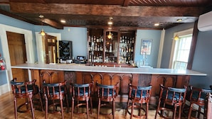 A bar area with a long counter, multiple stools, and a variety of bottles. - Arlington Inn (Arlington)