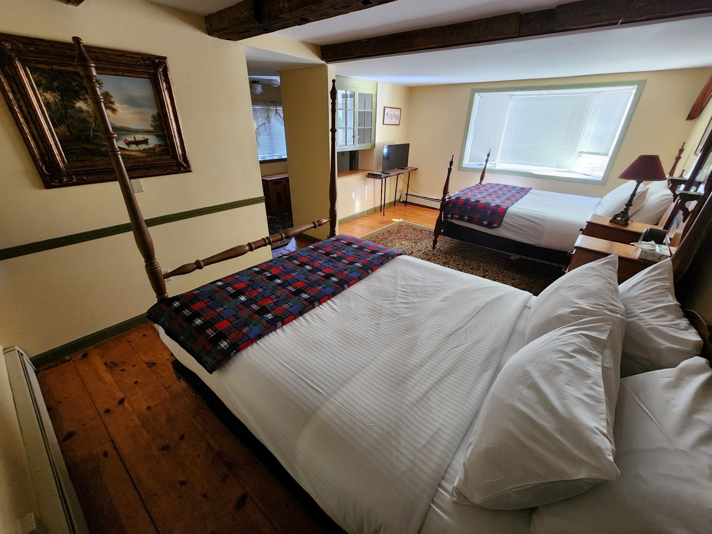 Ein Schlafzimmer mit zwei Betten, Holzboden, einem Bild an der Wand und einem Fenster mit Jalousien.