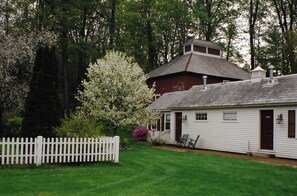 A white building with a red roof, surrounded by a white picket fence and lush greenery.