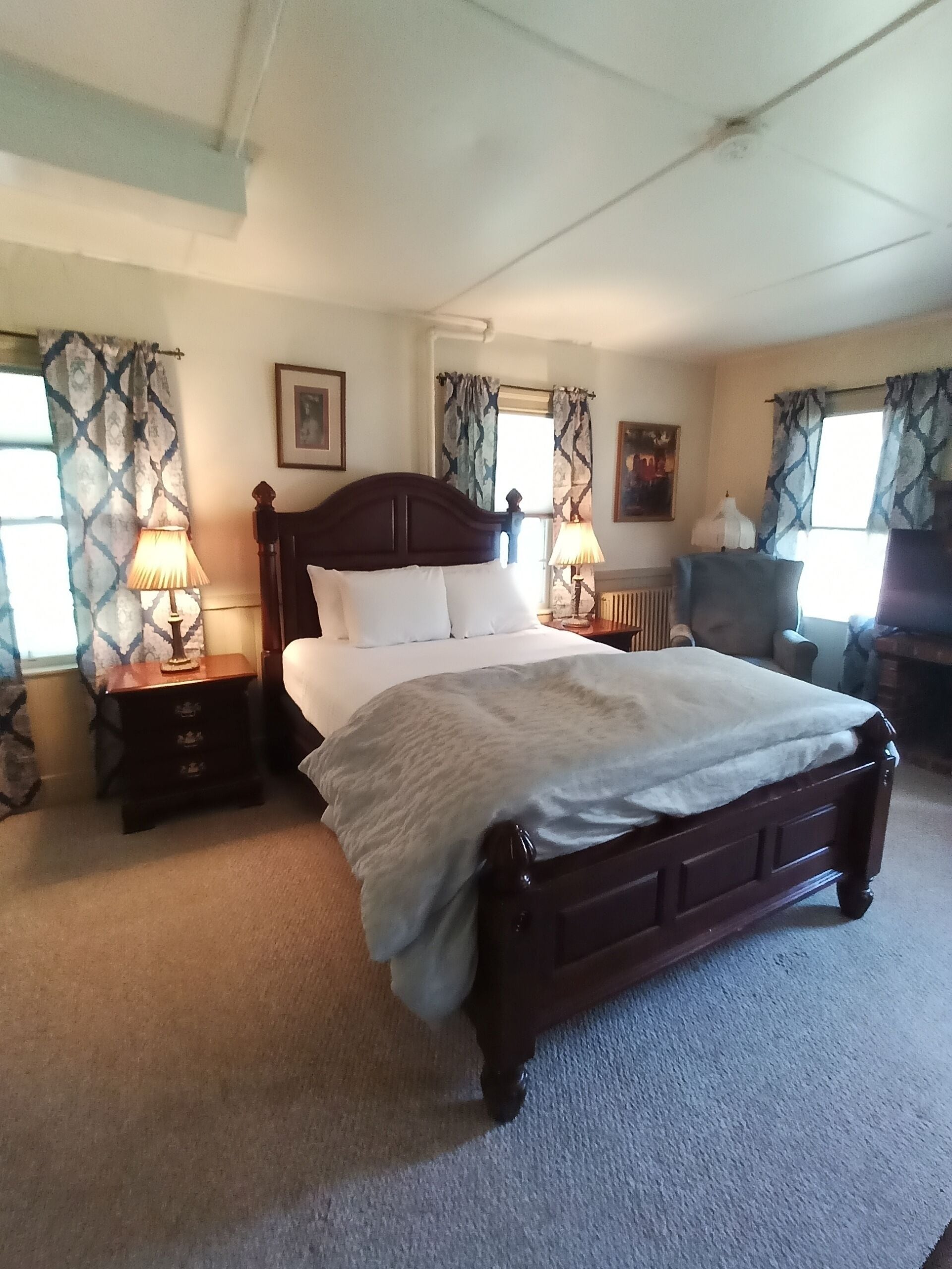 A neatly arranged bedroom with a large bed, two bedside tables with lamps, a dresser, and a chair.