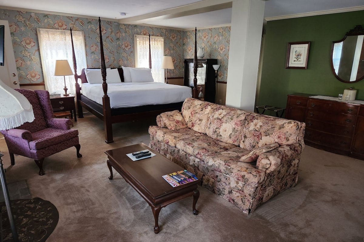 Une chambre à coucher avec un lit à baldaquin, un canapé à motifs floraux, une table basse en bois et une commode.