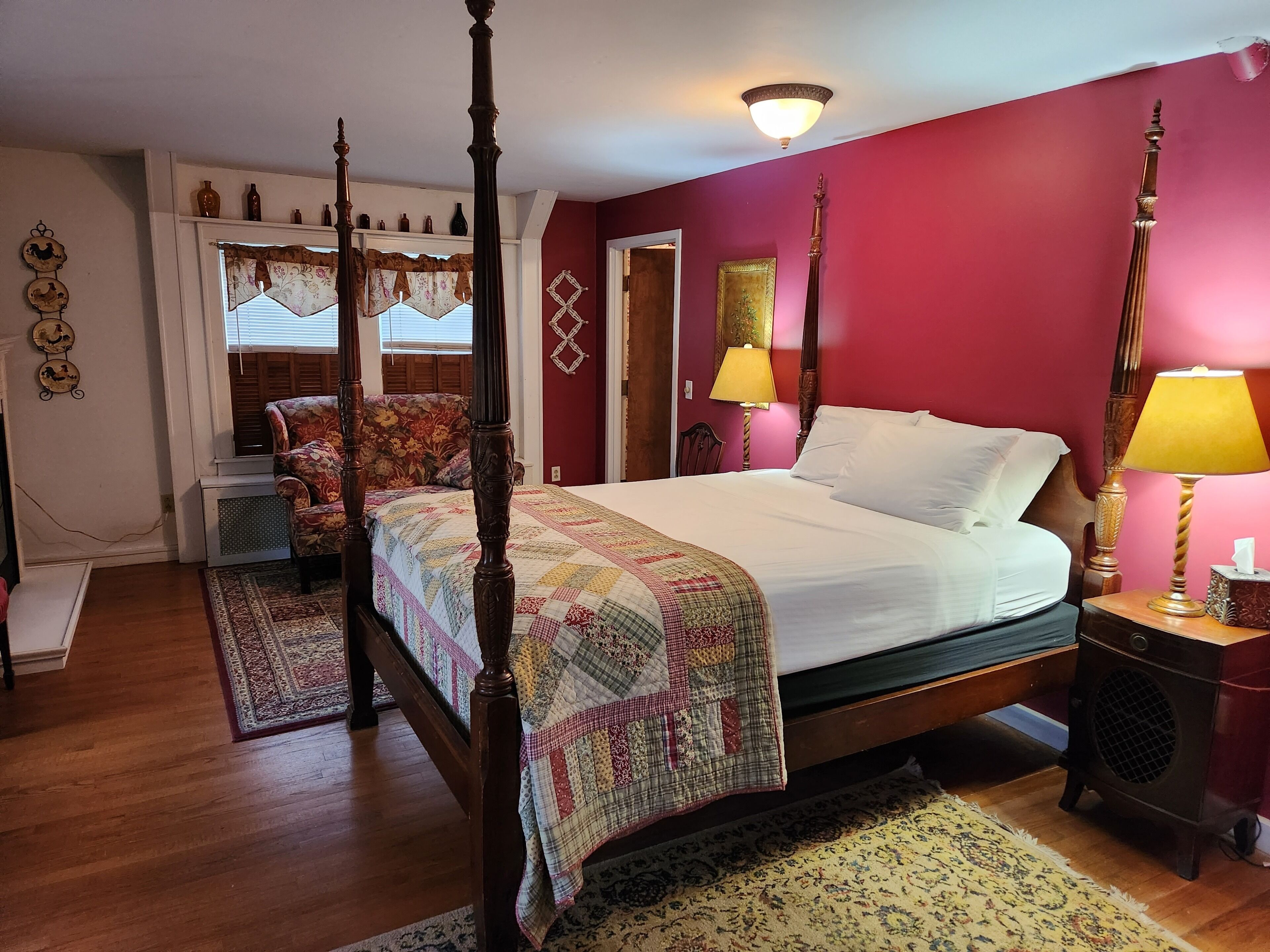 Una cama con dosel, un edredón, una mesita de noche con lámpara y un sillón con tapicería floral.