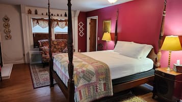 Una cama con dosel, un edredón, una mesita de noche con lámpara y un sillón con tapicería floral.
