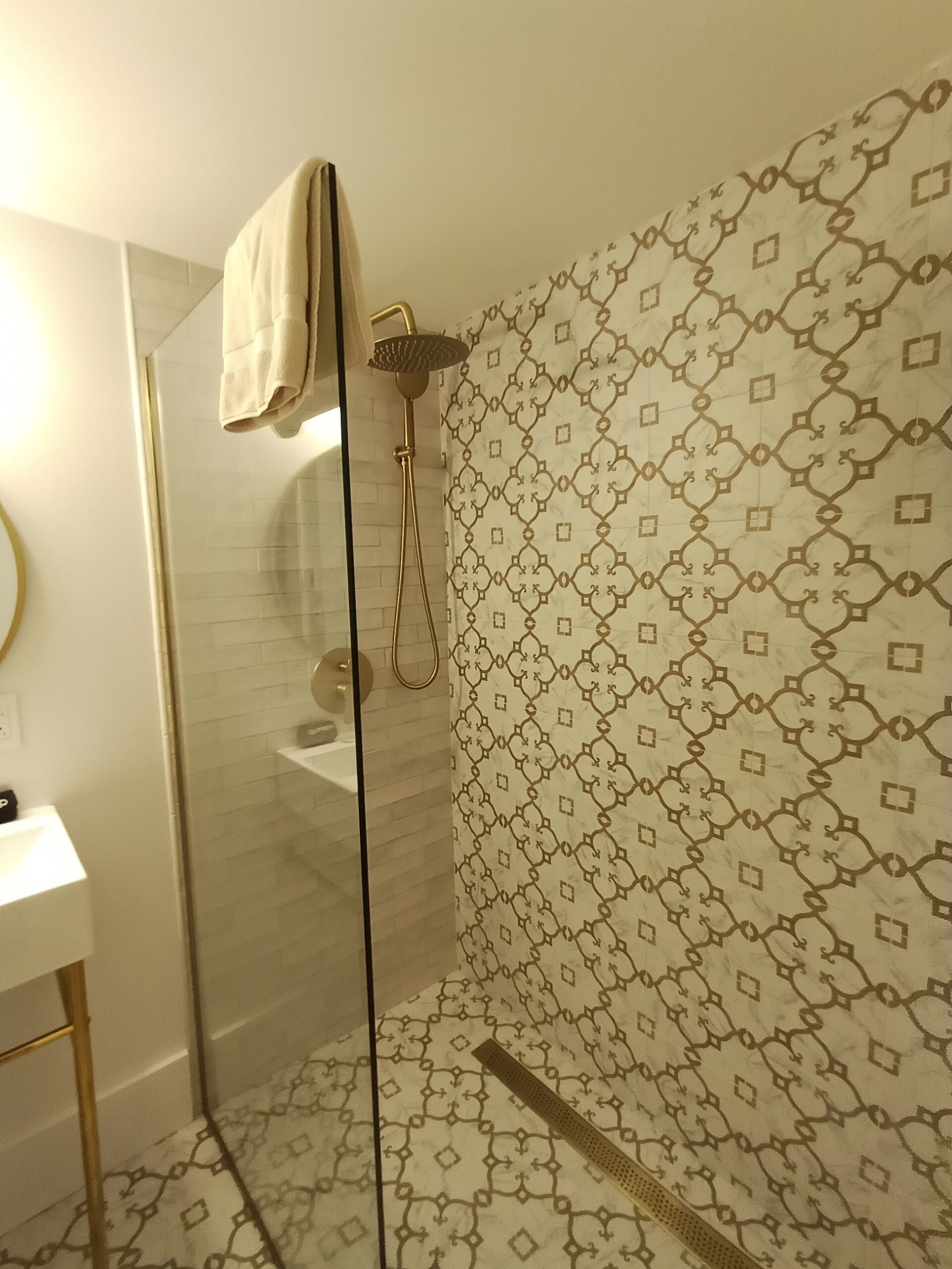 A bathroom with a glass shower enclosure, a white sink, and patterned wall tiles.