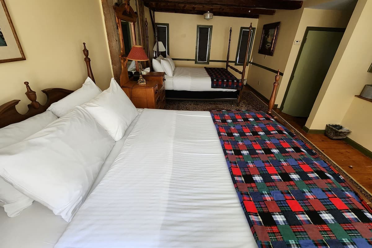 Une chambre d’hôtel avec deux lits, une tête de lit en bois, une courtepointe, une table de chevet, une lampe et un miroir.