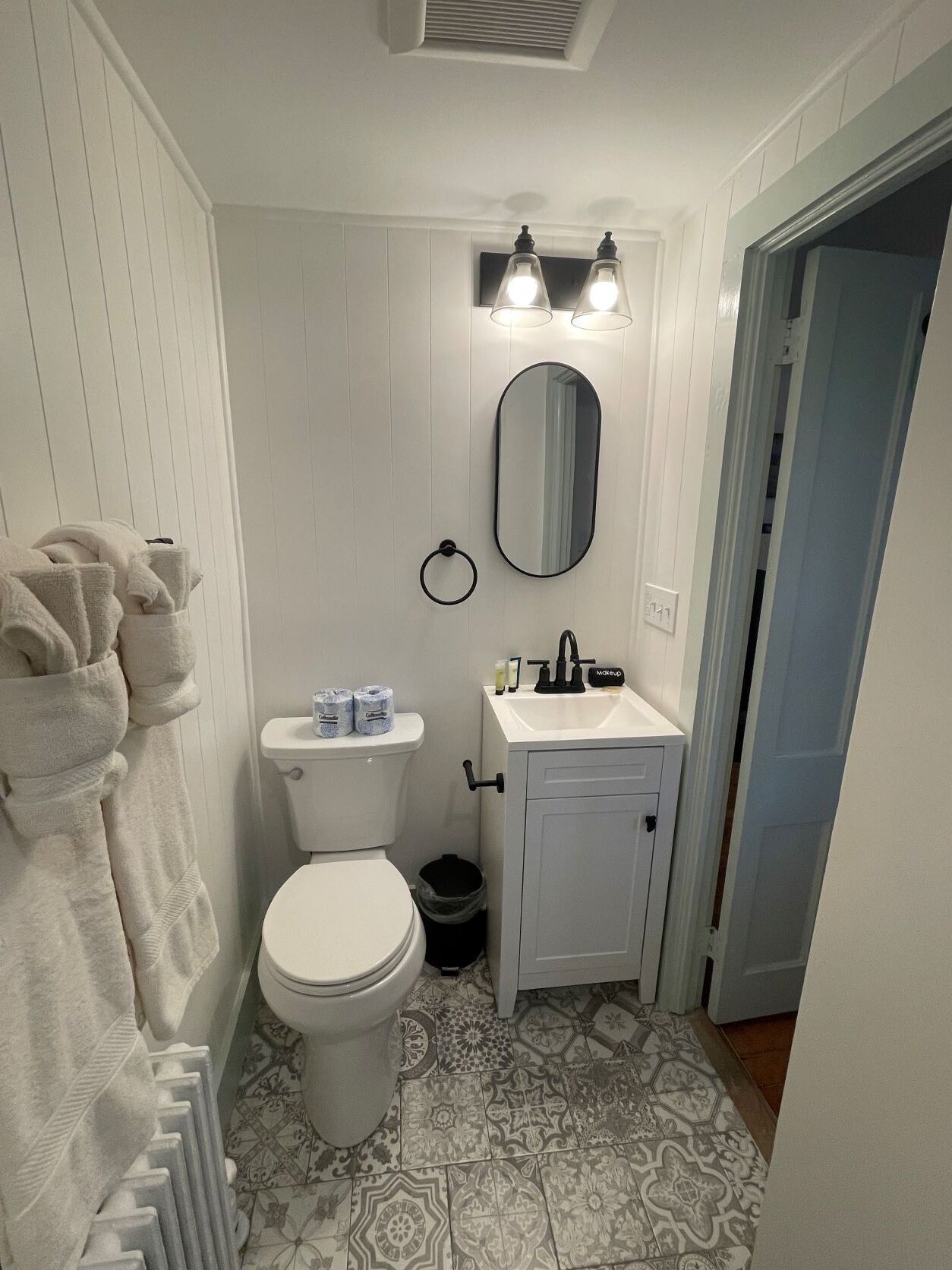 Une salle de bain avec des toilettes, un lavabo et un miroir. Des serviettes sont accrochées au mur et il y a un radiateur.