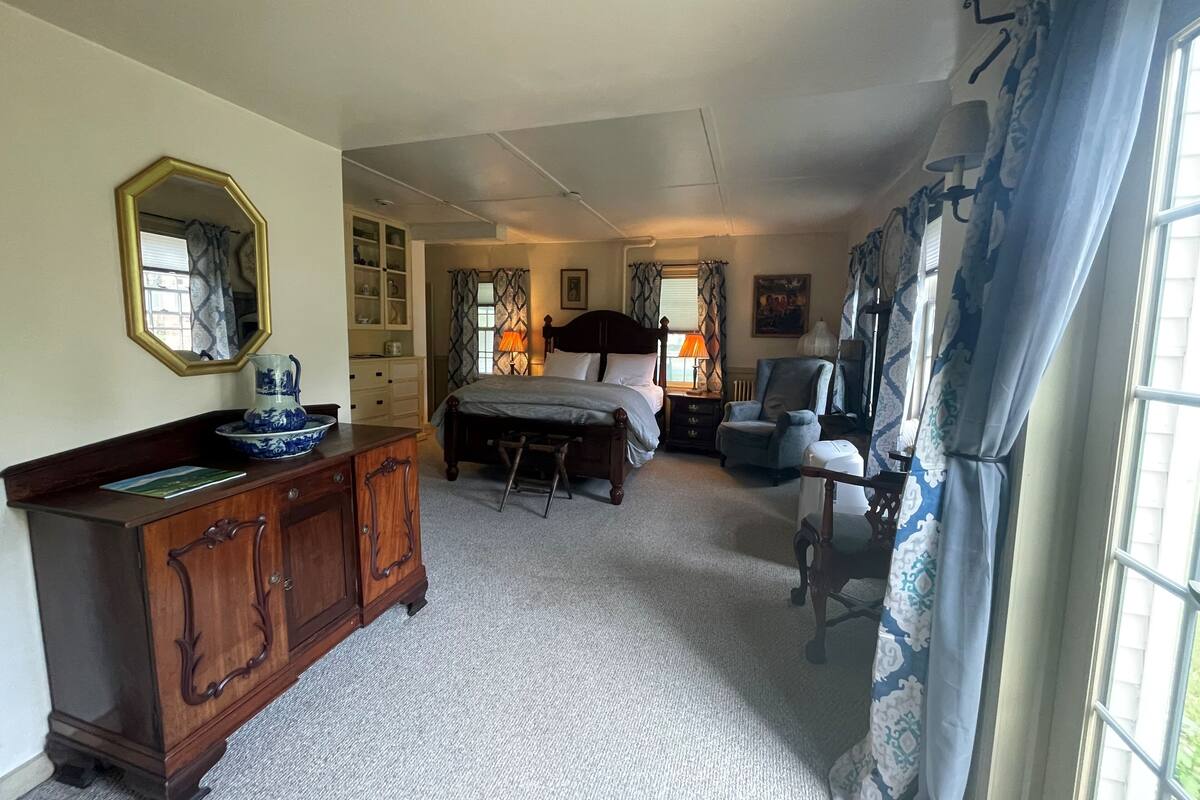 Une chambre à coucher avec un lit, une commode, une chaise et une fenêtre avec des rideaux.
