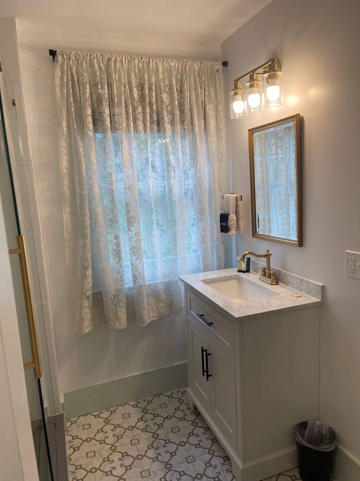 A bathroom with a sink, mirror, and window with a floral curtain.