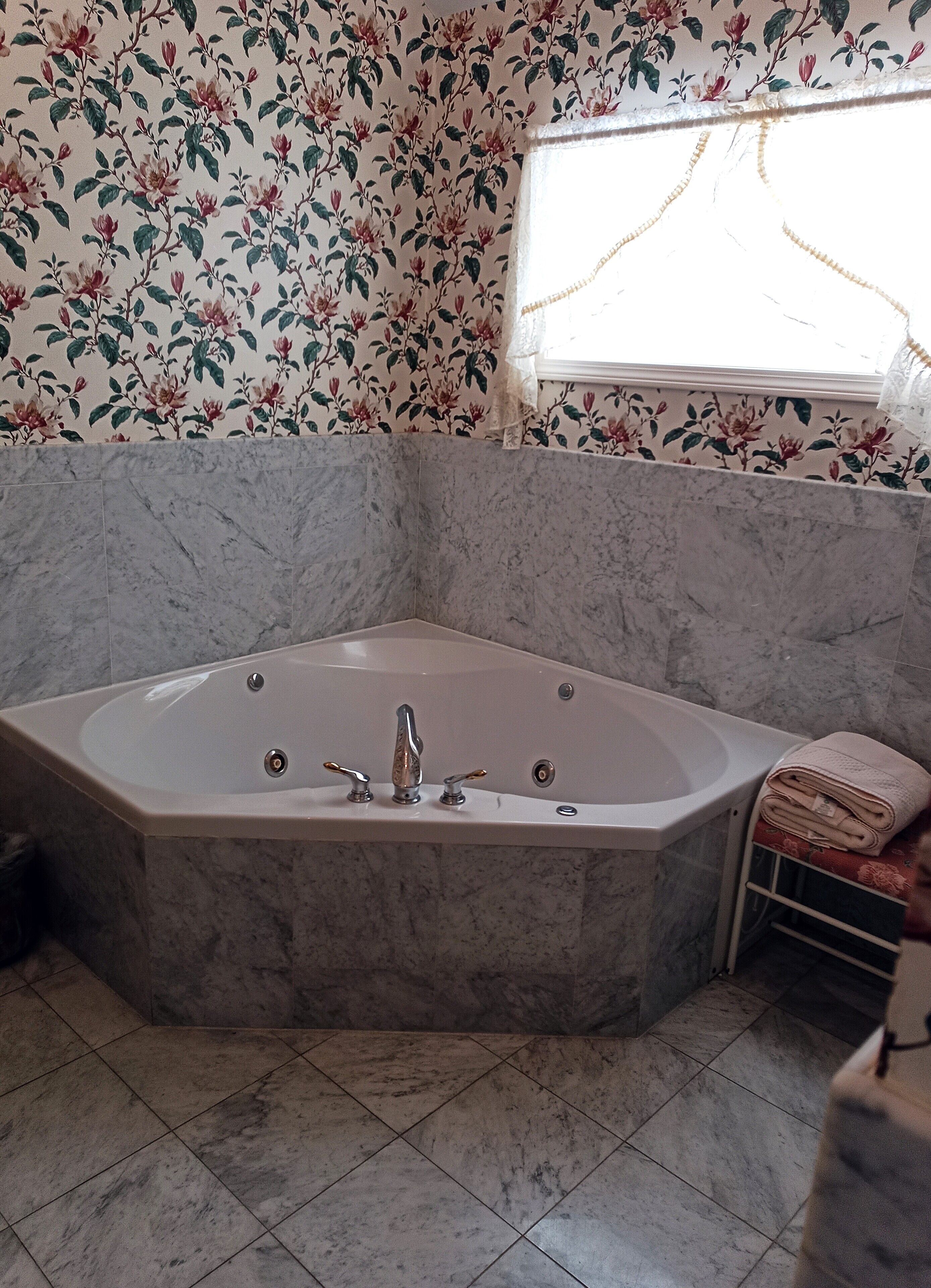 Un baño con una bañera independiente, baldosas de mármol y papel tapiz floral.