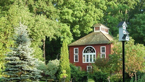 A red house with a white picket fence, surrounded by lush greenery and trees. - Arlington Inn (Arlington)