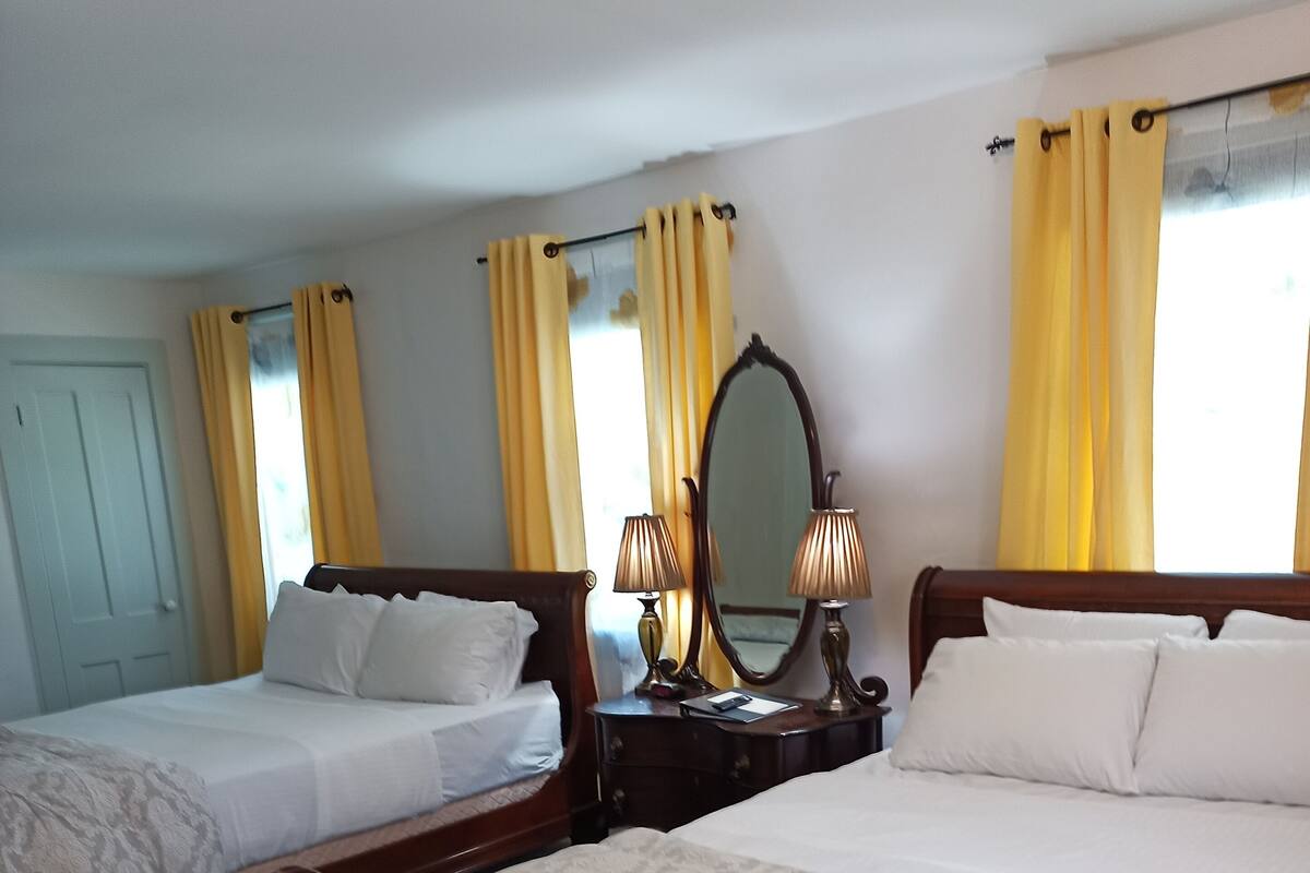 Une chambre d’hôtel avec deux lits en bois, une commode en bois, un miroir et des rideaux jaunes.