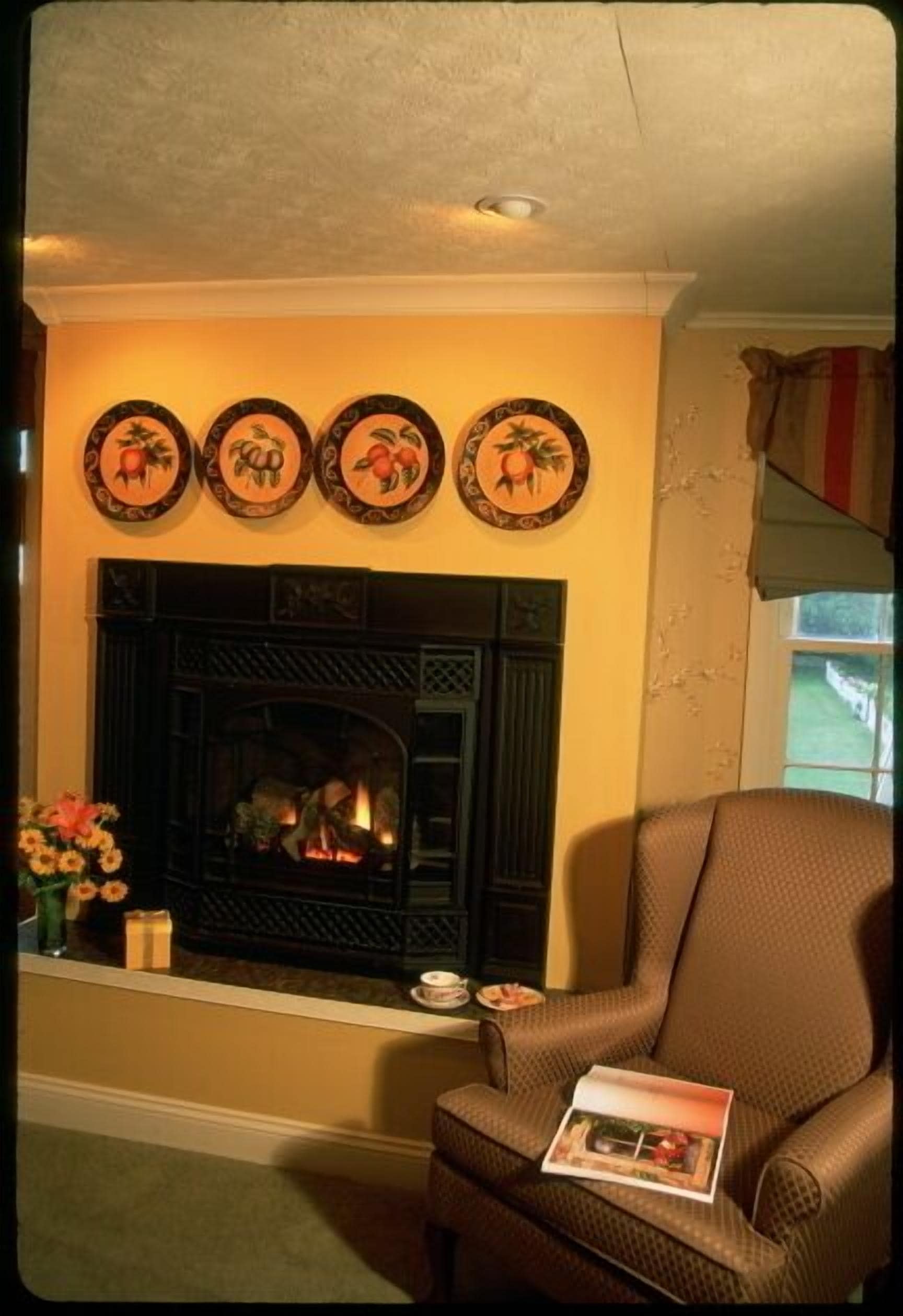 A living room with a fireplace, a brown armchair, and a vase with flowers.