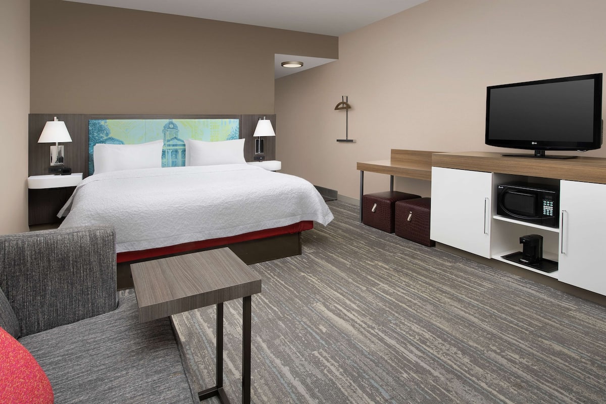 A hotel room with a bed, a TV, a microwave, a table, and a chair.