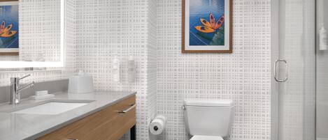 Un baño moderno con pared de azulejos blancos, tocador de madera, inodoro blanco y un cuadro enmarcado con kayaks.