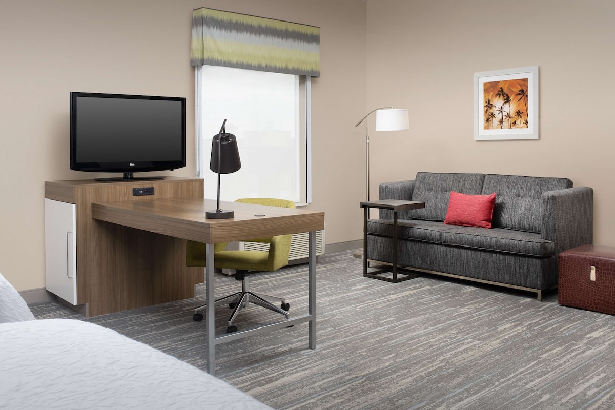 A hotel room with a desk, a television, a sofa, and a framed picture on the wall.