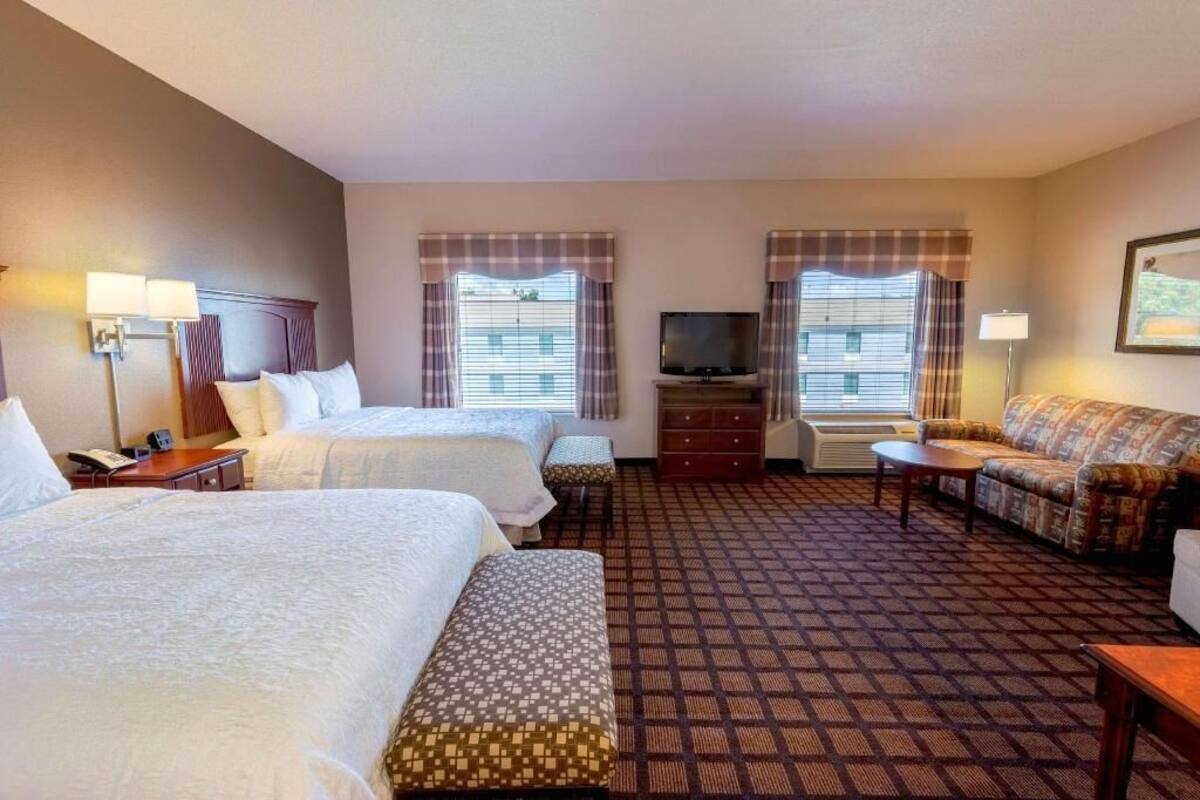 A hotel room with two beds, a sofa, a TV, and a desk.