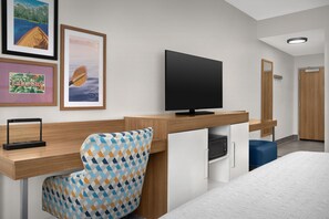 A hotel room with a wooden desk, a television, a patterned armchair, a bed, and framed pictures on the wall. - Hampton Inn & Suites Lake City (Lake City)