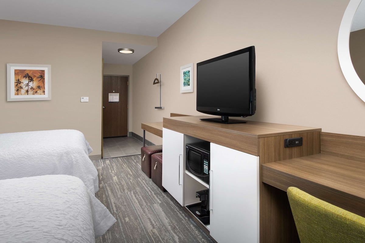 A hotel room with two beds, a desk with a flat-screen TV, a microwave, and a small seating area.