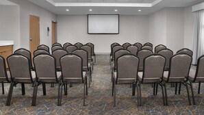 Una sala de conferències amb files de cadires, una pantalla de projector i un sòl amb moqueta.