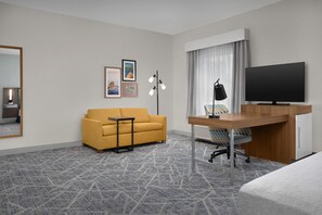 A hotel room with a sofa, a desk with a computer, a TV, a mirror, and framed pictures on the wall. - Hampton Inn & Suites Lake City (Lake City)