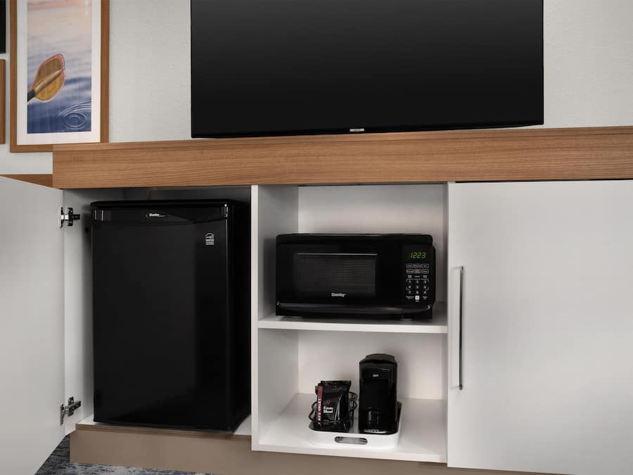 A kitchen with a refrigerator, microwave, and coffee maker on a white shelf.