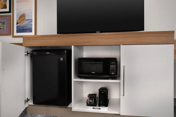 Una cocina con refrigerador, microondas y cafetera sobre un estante blanco.