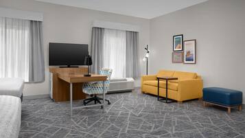 A hotel room with a bed, a desk with a computer, a sofa, a small table, and a TV.