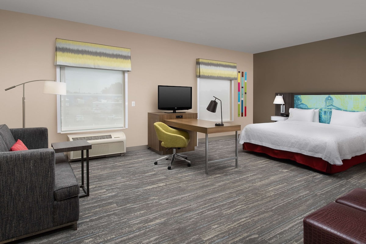 A hotel room with a bed, a desk with a computer, a chair, and a sofa.