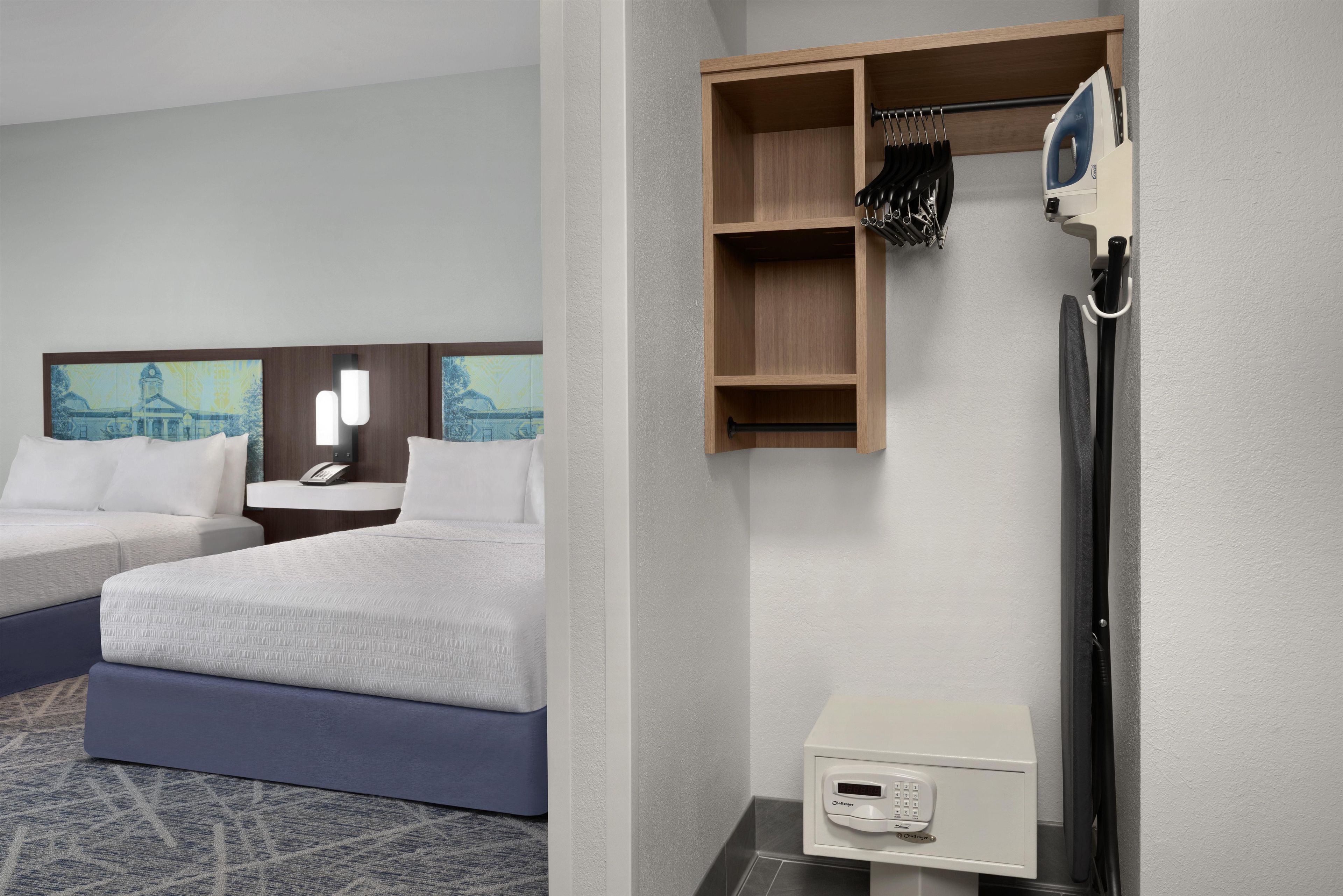 A hotel room with two beds, a desk, a telephone, a small cabinet, and a wall-mounted ironing board.