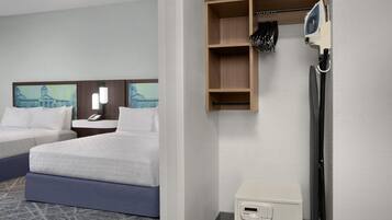 A hotel room with two beds, a desk, a telephone, a small cabinet, and a wall-mounted ironing board.