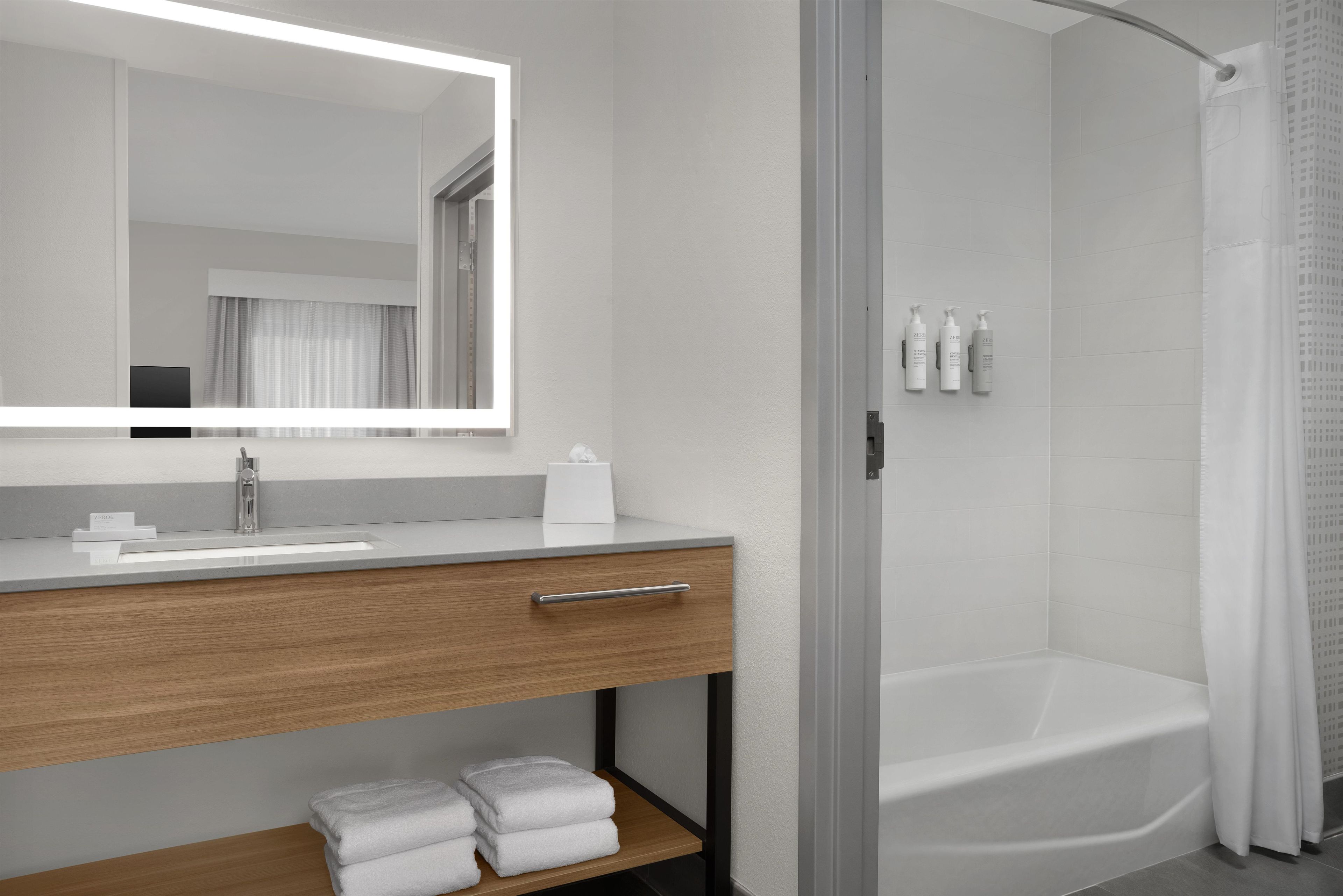 Un baño moderno con un espejo grande, un tocador de madera, una bañera y una zona de ducha.